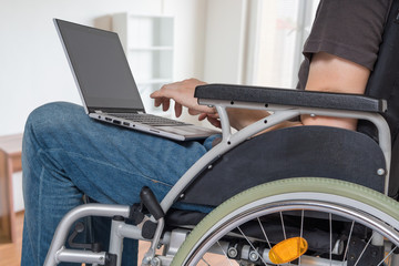 Handicapped disabled man on wheelchair is working with laptop in office.