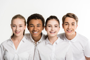 portrait of smiling multiethnic teenagers in white shirts looking at camera isolated on white