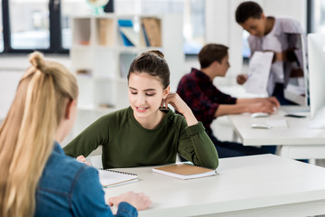 portrait of smiling teenage girl studying with friend together in class