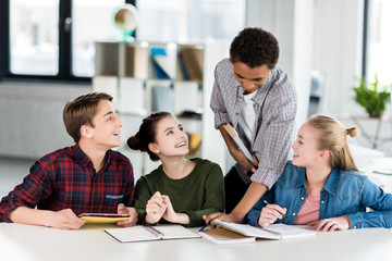 multiethnic group of teenagers doing homework together in class
