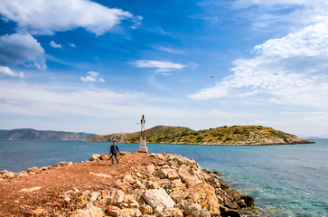 Boy walking a stone path leading to the a small metallic lighthouse. Pachi, Greece