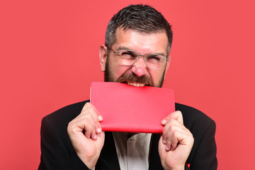 Guy bites closed notebook. Businessman with busy face and glasses