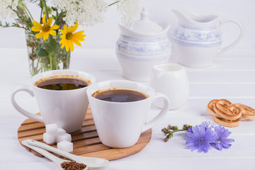 Obraz na płótnie Canvas Cup of coffee tea chicory drink hot beverage with chicory flower and sugar cookies on a white table. Still life with breakfast