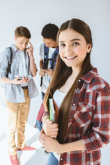 portrait of smiling teenage girl with notebook looking at camera with multiethnic boys standing behind isolated on white