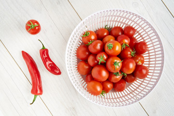 Fresh ripe red tomatoes and chillies in a colander on a pale wood work surface, worktop background