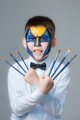 Little boy with paintings on his face Wolverine with brushes in hands