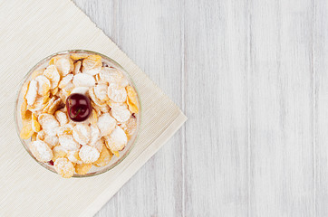 Healthy breakfast with golden corn flakes, ripe cherries, powdered sugar on white wood board top view, copy space.