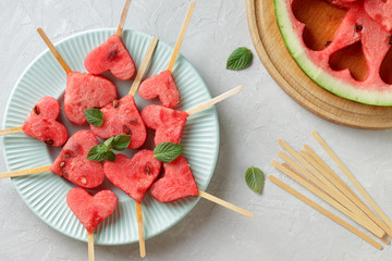 Watermelon heart popsicles on blue plate and wooden sticks and piece of watermelon on gray stone background. - 166987550