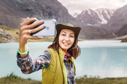 Tourist woman in hat taking picture with her smartphone in beautiful Mountain Lake in Altai