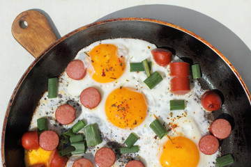 Hot sunny dish/ Frying pan with scrambled eggs in a rustic manner with fried sausage and fresh green onions