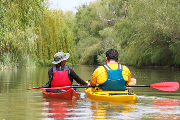Two man in red and yellow kayak in life jacket kayaking in Danube river on wild biosphere reserve in spring