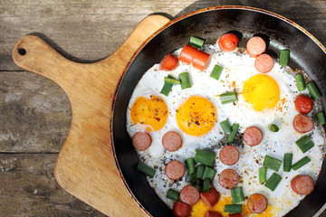 Rustic appetizing dish/ Hot fried eggs with sausages, herbs and seasoning, on an old wooden plank top view