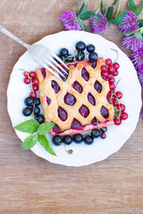 The cake with berry jam is served with red and black currants. Red clover flowers. Top view.