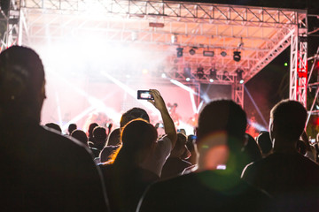 Rear view of crowd with arms outstretched at concert. cheering crowd at rock concert. silhouettes of concert crowd in front of bright stage lights. Crowd at music concert, audience raising hands up