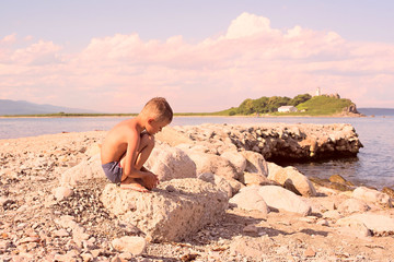 Fototapeta na wymiar The tanned boy sitting on the beach