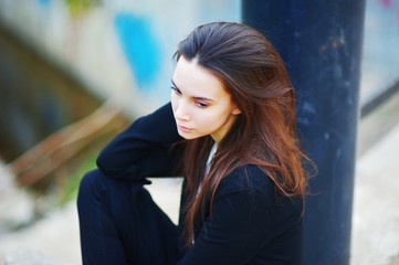 Obraz premium Portrait of pensive beautiful woman sitting on the street with a detached gaze. Close-up, blurred background.