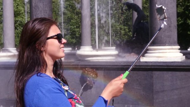 Girl takes a photo on the phone using a selfie stick on the background of a fountain and a beautiful rainbow. slow motion. 1920x1080. full hd