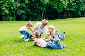 happy young family with two cute children resting together on green grass in park