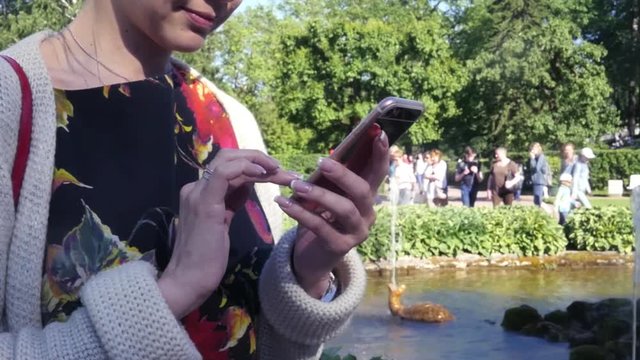 Girl with a phone in her hands is standing near a fountain in a park, close-up. slow motion. 1920x1080. full hd.