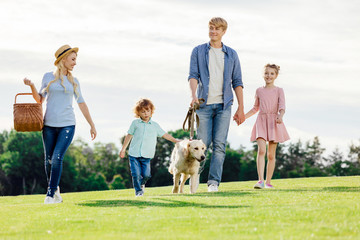 happy young family with two children walking with golden retriever dog in park