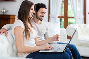 Young couple using a laptop sitting on their sofa