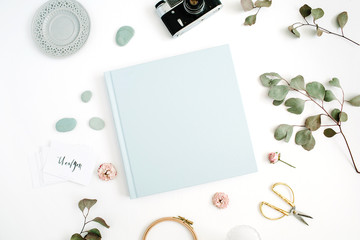 Fototapeta na wymiar Blue family or wedding photo album with blank space for text, eucalyptus leaf, retro camera and dry rose buds on white background. Flat lay, top view.