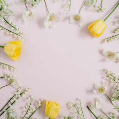 Frame of lily of the valley, yellow tulips, green leaves with space for text on pink background. Flat lay, top view