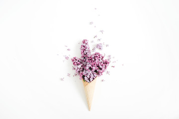 Obraz na płótnie Canvas Waffle cone with lilac flower bouquet on white background. Flat lay, top view floral background.