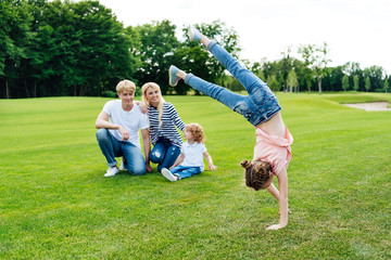 Obraz premium happy parents with son looking at cute little daughter performing handstand at park