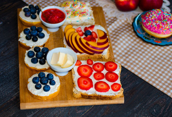 Delicious healthy breakfast, fruit sandwiches with different fillings, cheese, banana, strawberry, fishing, butter, blueberry, on a different wooden background.