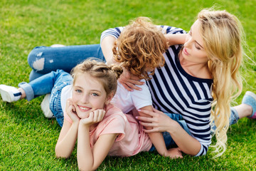 Fototapeta premium young mother with cute little children lying on green grass while resting in park