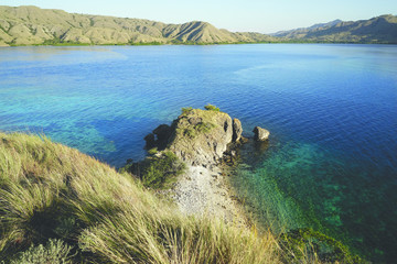 View from the top of a mountain at Gili Lawa overlooking other mountains at the coast with blue turquoise colored ocean water in between in Flores, Indonesia. © Eduard