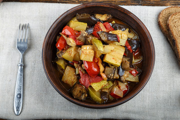 Vegetable stew with tomato, eggplant, zucchini, onion, carrot, pepper, close-up on a clay plate.