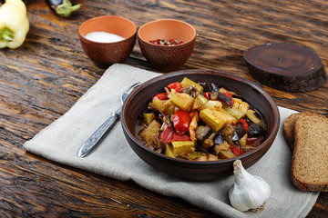 Vegetable stew with tomato, eggplant, zucchini, onion, carrot, pepper, close-up on a clay plate.