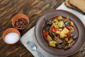 Vegetable stew with tomato, eggplant, zucchini, onion, carrot, pepper, close-up on a clay plate.