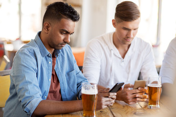 male friends with smartphone drinking beer at bar