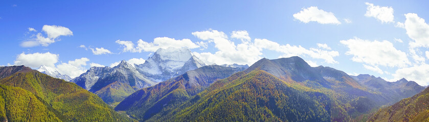 Shangri la, a panorama view of holy snow-clad mountain Chanadorje and yellow orange colored autumn trees in the valley in Yading national level reserve, Daocheng, Sichuan Province, China. - obrazy, fototapety, plakaty