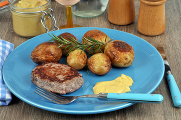 Assiette avec un steak haché, des pommes de terre et de la moutarde