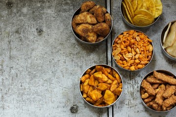 Variety of Indian snacks - Mixture, Tapiyoca chips, banana chips,Sarkara varatti, Sesame sticks served in metal bowls, top down view