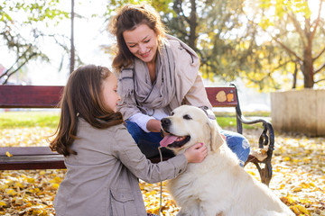 Family woman and her daughter walk autumn park,with his dog golden retriever