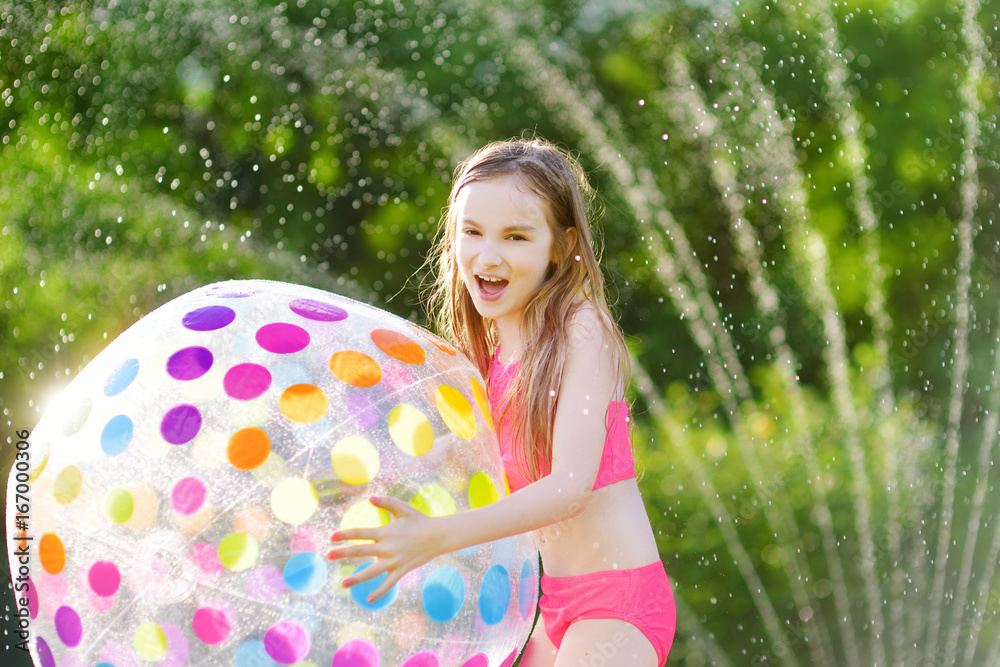 Sticker Adorable little girl playing with a sprinkler in a backyard on sunny summer day. Cute child having fun with water outdoors.