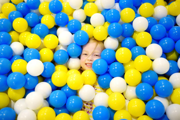 Happy little girl having fun in ball pit in kids indoor play center. Child playing with colorful balls in playground ball pool.