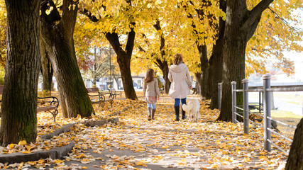 Family woman and her daughter walk autumn park,with his dog golden retriever