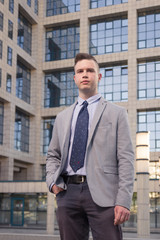 one young Caucasian man, blank expression, hand in pocket, business suit, formal wear, ordinary common person portrait, outdoor building exterior behind