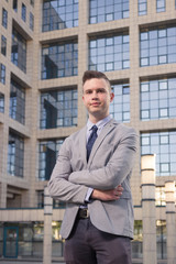 one young Caucasian man, cheerful expression, arms crossed, business suit, formal wear, ordinary common person portrait, outdoor building exterior behind