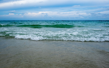 wave of green ocean on sandy beach and blue sky
