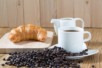 Coffee cup and croissant on wooden table