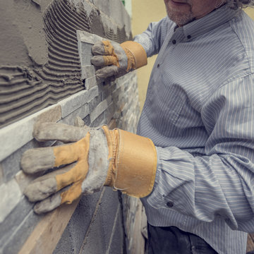 Worker pushing the tile into the cement on the wall