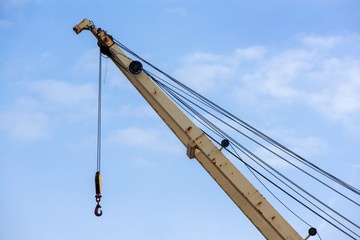 Shot of yellow boom with big hook, an old, rusty port crane preparing to lift cargo in ship on clear blue sky background. Equipment for unloading ships and barges, preparing for export world wide