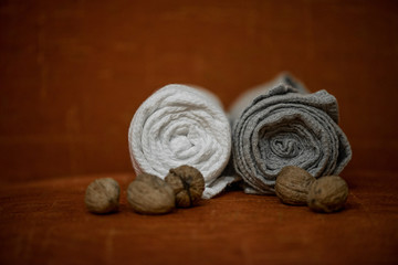 Macro shot of rolled, folded snow white and grey natural linen sauna and bath towels next to small walnuts on orange background, on massage table. Beautiful home decor, gift for newlyweds for wedding